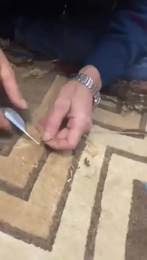 Mains tenant un outil fin et pointu au-dessus d'un tapis crème à motif de grecque brun