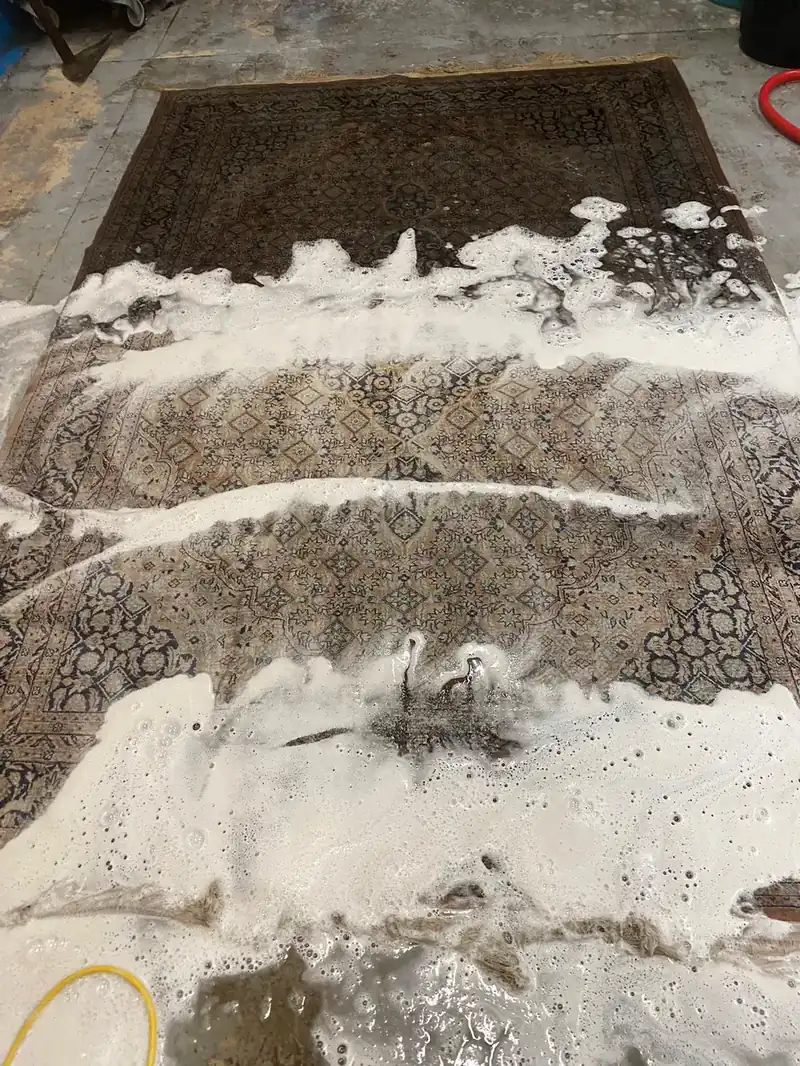 Grand tapis à motifs bleu nuit et beiges posé sur un sol gris, recouvert par endroits de mousse blanche