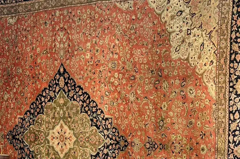 Détail d'un tapis à fond rouge orangé, médaillon vert et noir, bordure bleu nuit et fins motifs de fleurs
